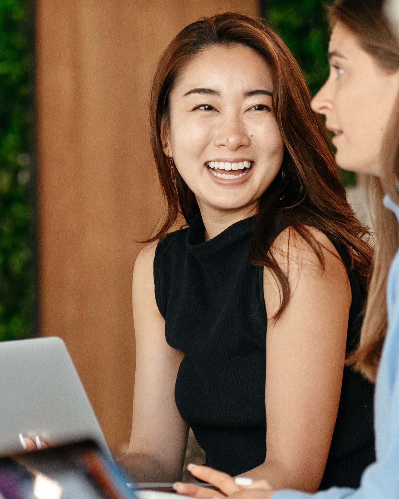 Two colleagues laughing together over a laptop in a bright office.